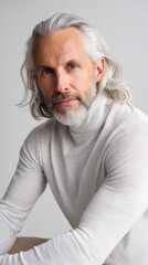 A man with flowing silver hair in a minimalist turtleneck staring at the camera with calm intensity in a white studio setting. 