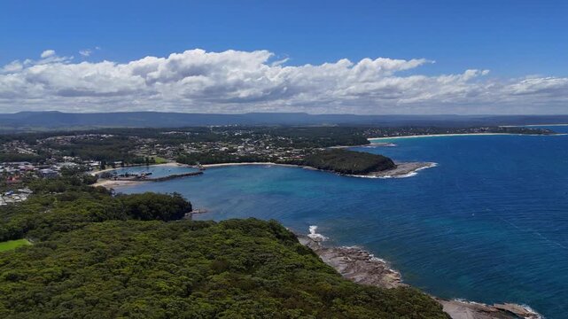 Coastal headland estabilshing rocky points and rolling surf beside lush green shoreline in Ulladulla, aerial