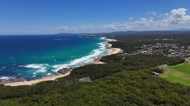 Turquoise surf lines wrap around rocky points with dense greenery framing Ulladulla coastline, panoramic overview Australia establishing