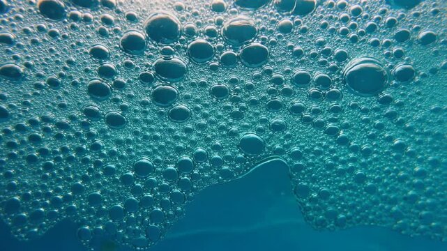 Macro close-up of a vibrant turquoise liquid surface covered in countless iridescent bubbles, creating an abstract and dynamic foam texture that highlights the physics of surface tension
