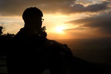 Fototapeta premium Silhouette of Man Sitting and Watching Sunset Over Valley
