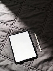 Blank tablet screen mockup with stylus on quilted bed fabric flat lay 