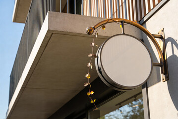 Round hanging storefront sign blank mockup on modern building facade with vine detail