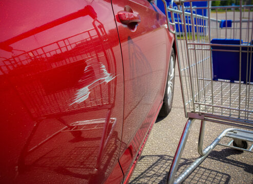 Parked red vehicle with paint damage done by shopping cart