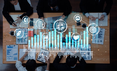 Group of professionals engaged in a business meeting analyzing data charts while digital icons represent themes of innovation and growth in modern office space. Trope