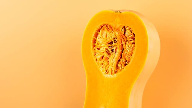 A close-up shot of a halved, orange squash with seeds, set against a monochromatic background