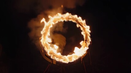 Dramatic nighttime shot captures a fiery ring of intense orange flames suspended in darkness suggesting a dangerous stunt or magical portal effect