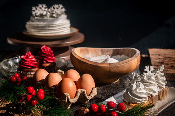 A cozy holiday atmosphere unfolds as baking begins, with a wooden bowl surrounded by eggs, cupcakes, Christmas decorations, and various ingredients—perfect for a Christmas and New Year's cooking theme