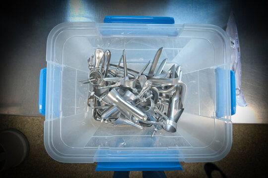 A collection of sterilized gynecological speculums and medical examination instruments stored inside a transparent plastic container.