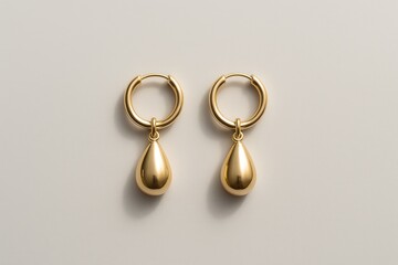 A pair of elegant gold drop earrings with teardrop shapes displayed on a neutral beige background, radiating modern luxury