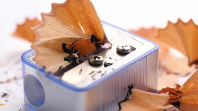 Close up of a pencil sharpener with wood shavings against white backdrop