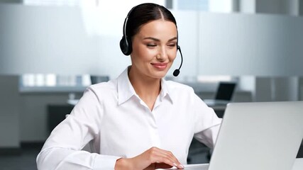 A friendly call center agent with a headset speaks while using a laptop