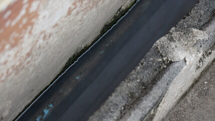 Narrow Concrete Drainage Channel with Water Flowing Between Weathered Walls