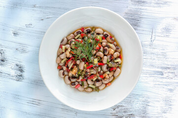 A top-down view of black-eyed peas cooked in olive oil, served as a traditional Mediterranean mezze on a white plate over a rustic wooden background.