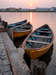 Two wooden boats on a river at sunset with serene reflections.