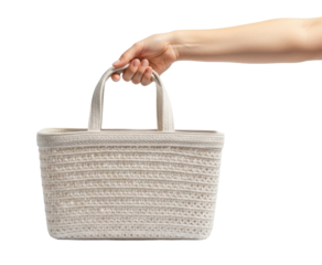 A person's hand holding a beige woven basket with two handles, isolated on white.