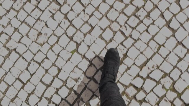 Top down cinematic view of walking on traditional Portuguese calcada pavement stones during daytime with smooth stabilized movement and textured urban detail.