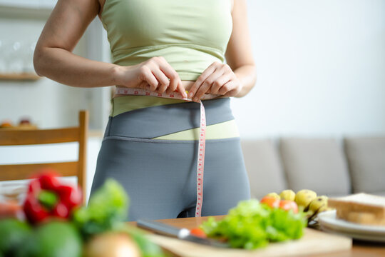 Weight loss and fitness concept of woman measuring waist at home. Healthy lifestyle, diet plan, body measurement, nutrition and wellness routine