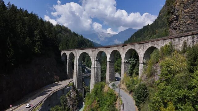 Drone flying upwards towards an old French bridge with roads underneath in 4k