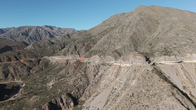 Aerial view of grey-paved section of Ruta 40 RN, contrasting dramatically with deep red and ochre geological formations color-rich mountains of the Cuesta de Miranda in Chilecito, La Rioja, Argentina