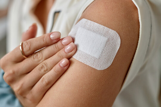 Woman touching adhesive bandage on upper arm, showing manicured hand with natural nails, birth control concept
