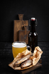 Dried roach fish and glass of beer on dark table, flat lay