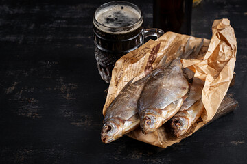 Dried roach fish and glass of beer on dark table, close up