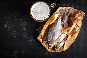 Dried roach fish and glass of beer on dark table, flat lay