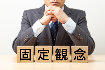 「固定観念」と書かれたブロックとビジネスマン
