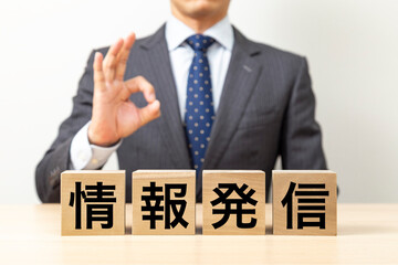 「情報発信」と書かれたブロックとOKポーズをするビジネスマン