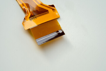 Macro shot of an orange flexible printed circuit (FPC) cable on a white background. Electronic component showing gold contact pins and internal traces for data transmission.