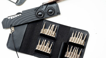 Top-down view of a black internal speaker module and a bronze precision screwdriver placed above an open black leatherette carrying case holding rows of interchangeable screwdriver bits.