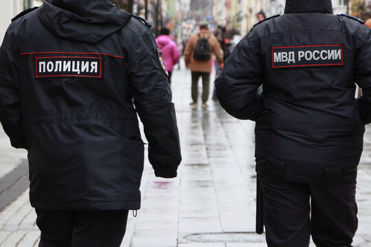 Back View Of Two Police Officers In Uniform With Russian Text Police And MVD Russia Walking On A Wet Pavement. Concept Of Law Enforcement And Safety.