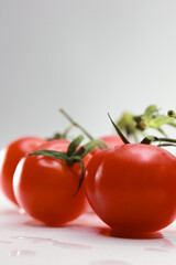 Macro Shot Of Glossy Red Tomatoes Attached To A Green Stem. The Image Emphasizes The Vibrant Color And Smooth Skin Of The Fresh Vegetables.