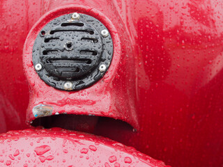 Close up of a wet surface old red classic scooter with a black horn with water drops.