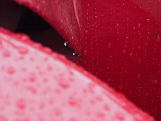 Water drops on a red metal surface with blur out of focus foreground.
