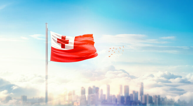 Tonga flag wavering in beautiful clouds with building skyline. The flag with drone shot in beautiful sky. Tonga national flag for independence day. - Powered by Adobe