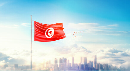 Tunisia flag wavering in beautiful clouds with building skyline. The flag with drone shot in...