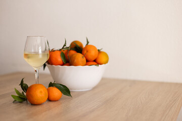 A glass of cold white wine next to tangerines on the wooden table.