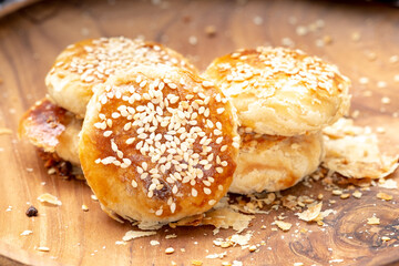 Traditional Indonesian bakpia pastry with mung bean filling on a wooden plate. Close-up high-angle shot of a flaky snack with crumbs and a checkered cloth detail.