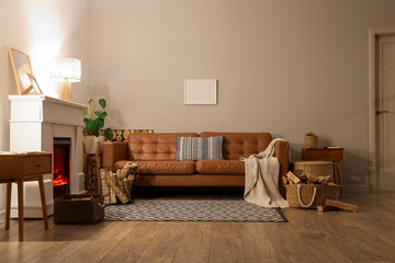Fototapeta premium Interior of living room with sofa, glowing lamps, bedside tables and firewood near fireplace in evening