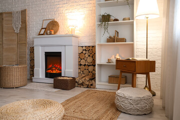 Fototapeta premium Interior of living room with shelving unit, folding screen, wicker coffee table and firewood near fireplace