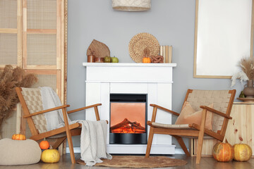 Fototapeta premium Interior of living room with armchairs, closet and autumn decorations on fireplace