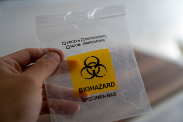 Hand holding biohazard specimen bag with warning symbol
