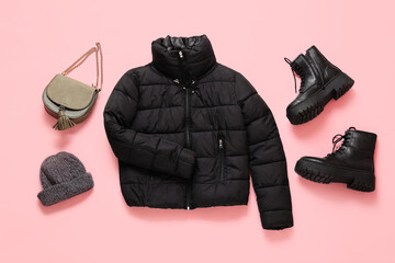 Stylish short black puffer jacket with boots, bag and winter hat on pink background
