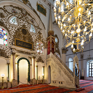 Interior of Hisar Mosque, Izmir, Turkey, showcasing ornate mihrab, minbar, grand chandeliers, stained glass windows, and intricate Islamic calligraphy
