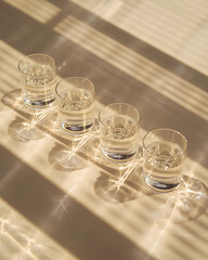 Minimal still life of clear water glasses casting long shadows in warm sunlight, creating a calm modern composition focused on hydration, balance, and simplicity