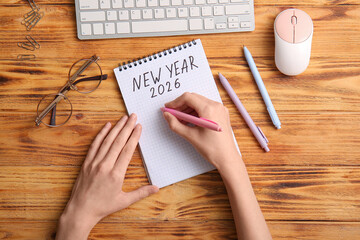 Woman with keyboard writing plans on 2026 against brown wooden background