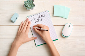 Woman with computer mouse and stationery writing new years goals against white wooden background