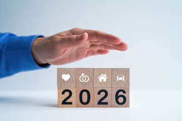 Hand protects wooden blocks showing icons for 2026 year planning and financial security.